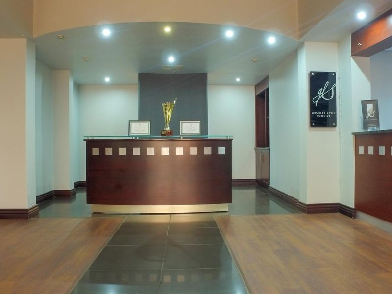 A professional office reception area featuring a built-in wooden reception desk, recessed lighting, and a combination of laminate and tiled flooring.