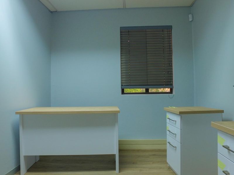 A functional office space featuring light blue walls, laminate flooring, and venetian blinds, providing a clean and professional work environment.