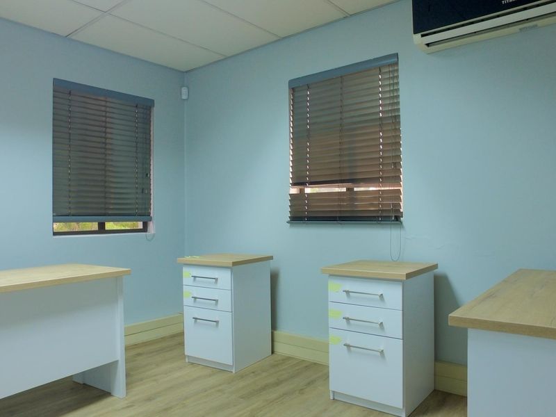 A functional office space featuring laminate flooring, a suspended ceiling, split-system air conditioning, and windows fitted with venetian blinds.