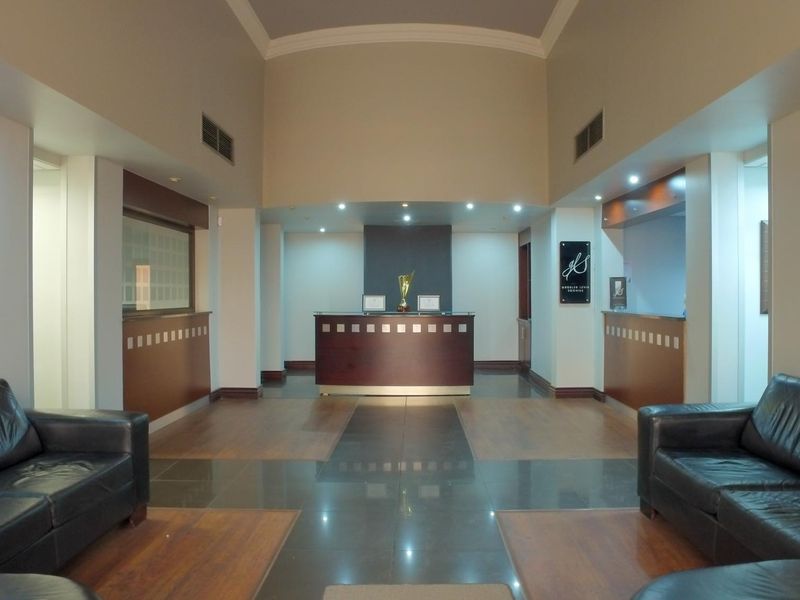 A professional office reception area featuring a central reception desk, high ceilings with cove lighting, and a combination of tiled and wood laminate flooring.