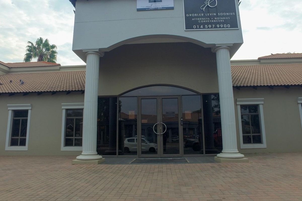 Front facade of a professional office building featuring a paved entrance, decorative columns, and glass double doors.