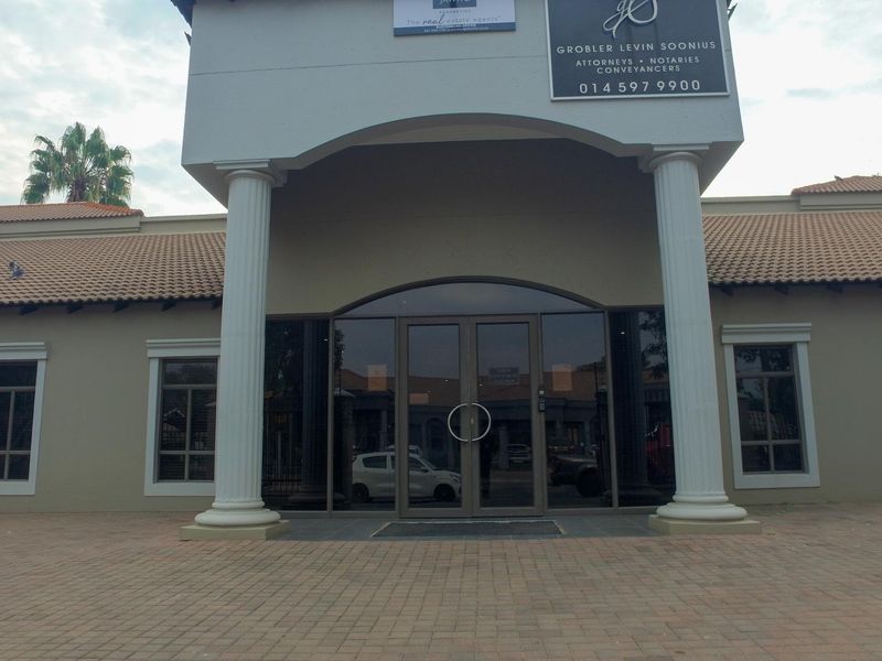 Front facade of a professional office building featuring a paved entrance, decorative columns, and glass double doors.
