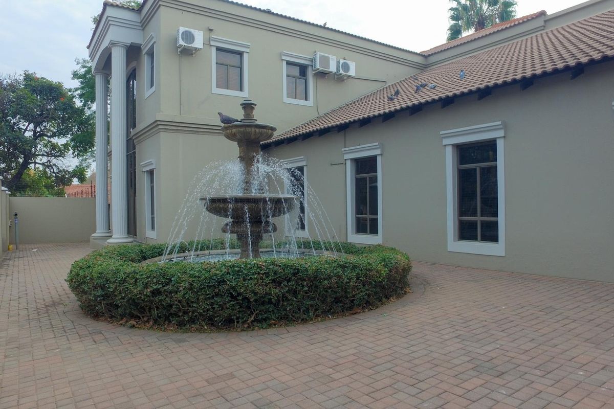 A well-maintained office courtyard featuring a central stone fountain, paved flooring, and classic architectural columns against the building facade.