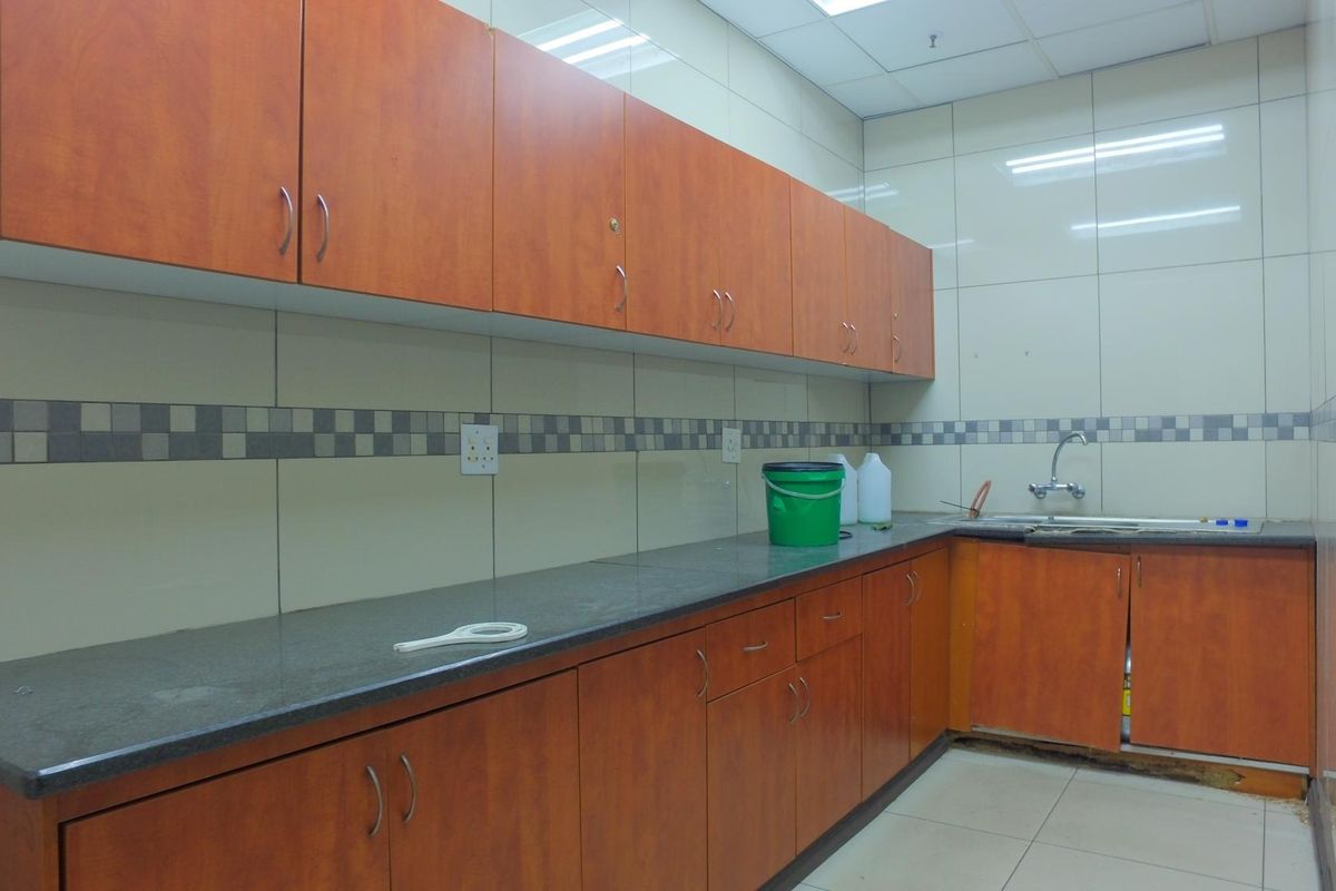 A functional industrial kitchen area featuring laminate cabinetry, stone countertops, a stainless steel sink, and tiled wall finishes.