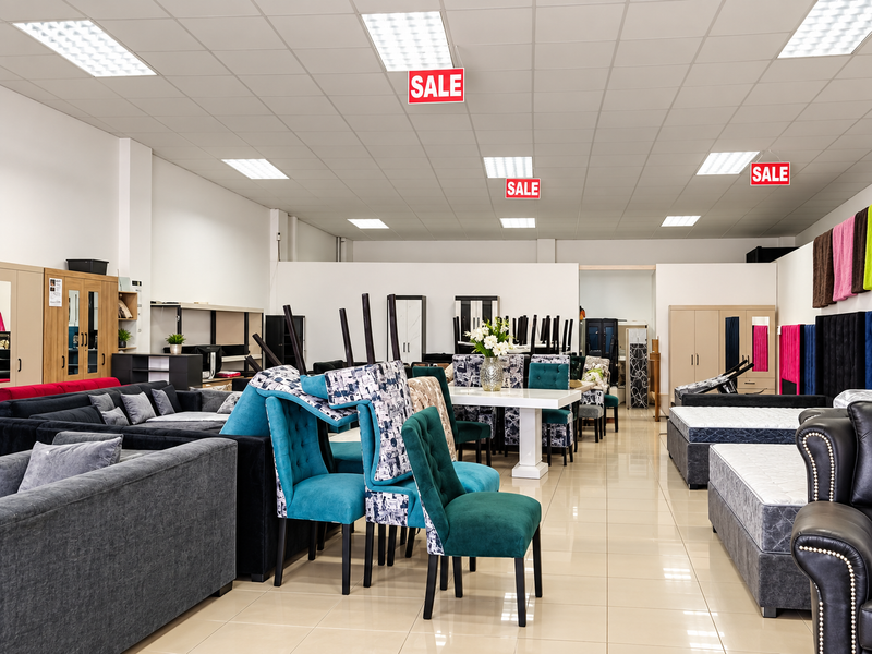 Spacious retail showroom featuring a suspended ceiling with recessed lighting and polished tiled flooring, currently utilized for furniture display.