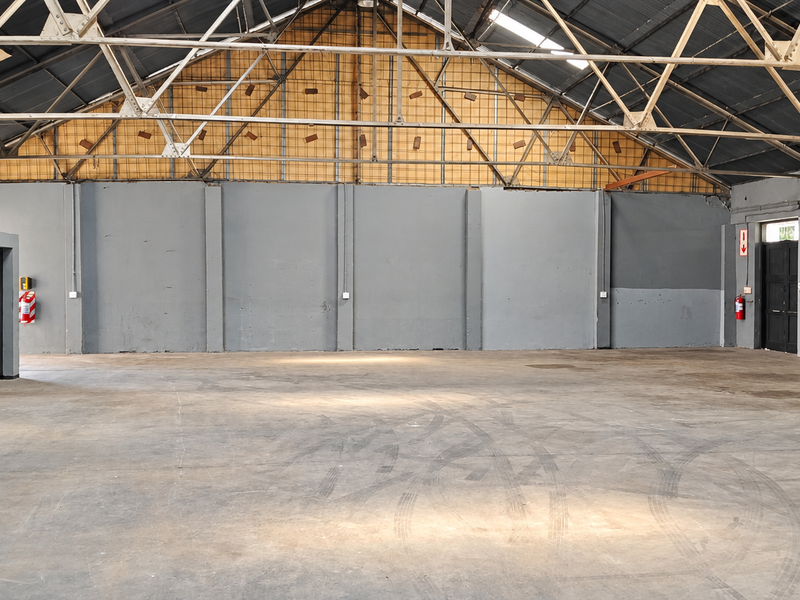 Spacious industrial warehouse featuring high exposed steel roof trusses, durable concrete flooring, and multiple access points, suitable for various commercial or storage applications.
