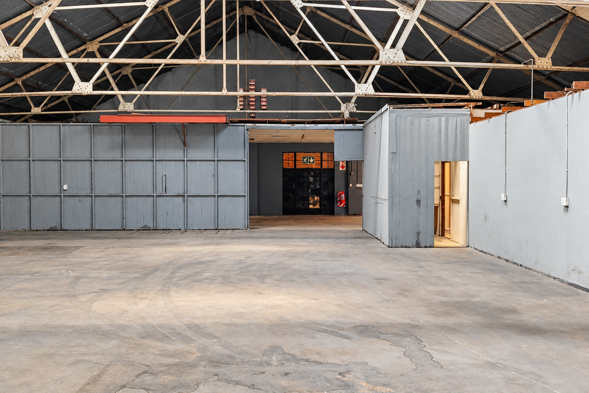 Spacious industrial warehouse area featuring exposed steel roof trusses, concrete flooring, and a partitioned office enclosure, suitable for various commercial or storage applications.