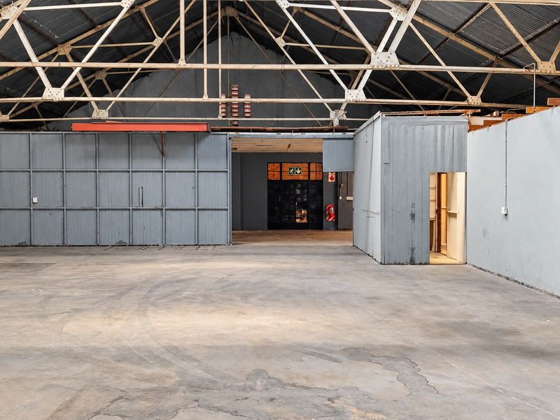 Spacious industrial warehouse area featuring exposed steel roof trusses, concrete flooring, and a partitioned office enclosure, suitable for various commercial or storage applications.