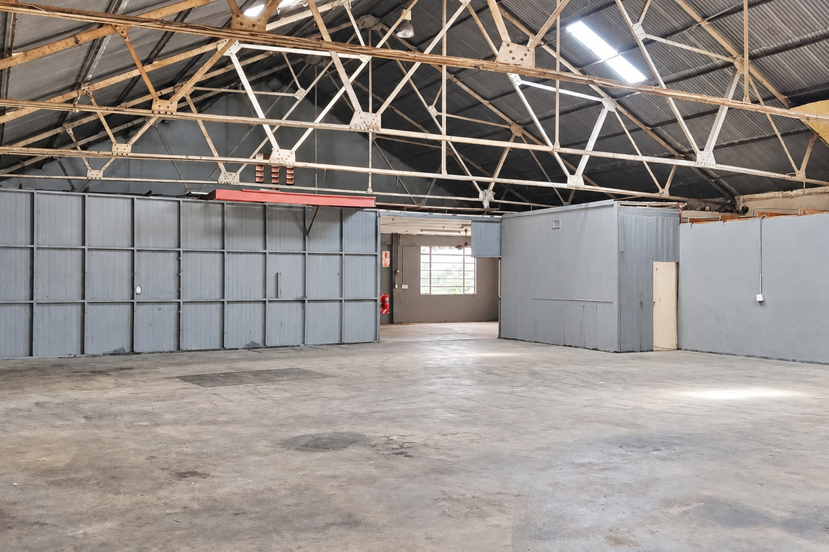 Spacious industrial utility area featuring high exposed steel roof trusses, concrete flooring, and partitioned office space, suitable for various commercial or storage applications.
