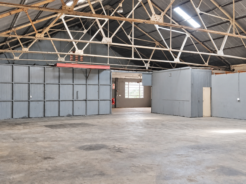 Spacious industrial utility area featuring high exposed steel roof trusses, concrete flooring, and partitioned office space, suitable for various commercial or storage applications.