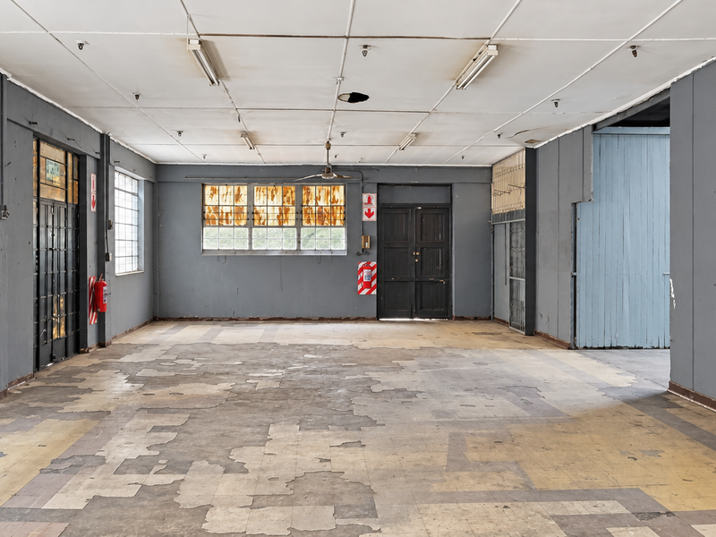 Spacious industrial open-plan area featuring high ceilings, fluorescent lighting, and significant flooring wear, suitable for versatile commercial or warehouse use.