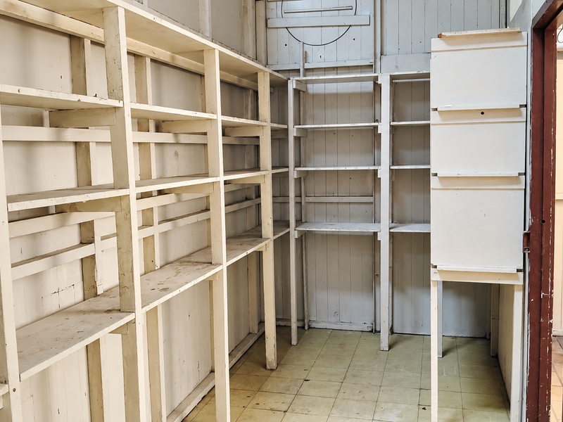 A functional utility or storage room featuring extensive built-in timber shelving, tiled flooring, and vertical timber wall paneling.