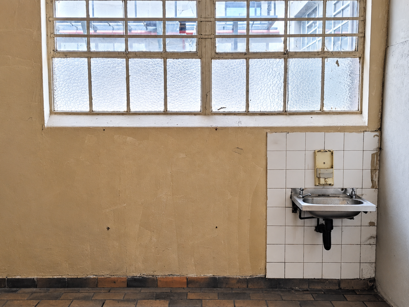 A functional utility space featuring a wall-mounted stainless steel basin, tiled splashback, and industrial-style steel-framed windows with tiled flooring.