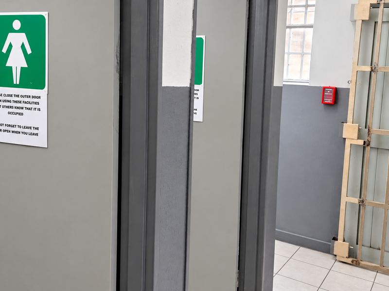 Industrial bathroom facility featuring secure metal gates, tiled flooring, and clearly marked access doors.