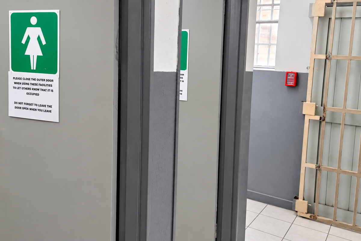 Industrial bathroom facility featuring secure metal gates, tiled flooring, and clearly marked access doors.