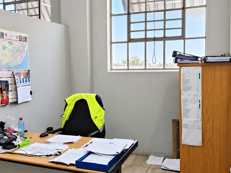 A functional industrial office space featuring tiled flooring, a partition wall, and large steel-framed windows providing natural light.