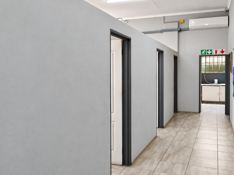 A clean, well-maintained industrial hallway featuring tiled flooring, partition walls, and an integrated air conditioning unit, leading to a secondary utility area.