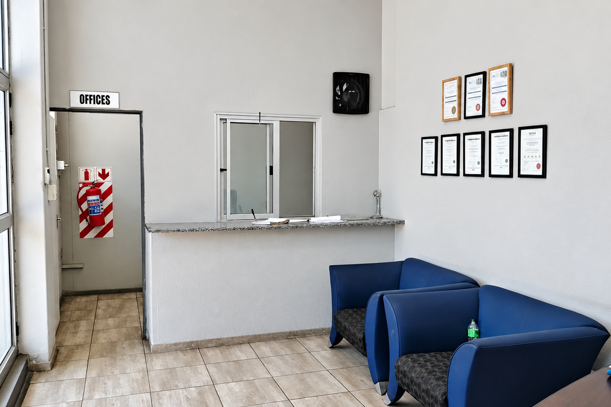 A functional industrial reception area featuring a service counter, tiled flooring, and a dedicated office access point with safety equipment.