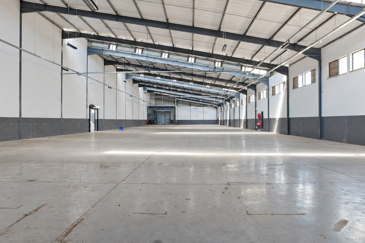 Spacious industrial warehouse featuring high ceilings, exposed steel portal frame, polished concrete flooring, and ample natural light through side windows.