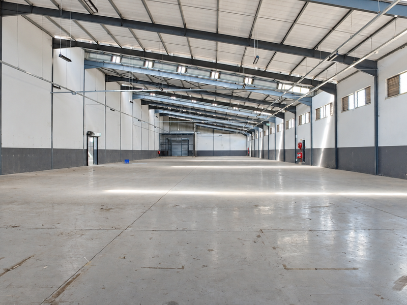 Spacious industrial warehouse featuring high ceilings, exposed steel portal frame, polished concrete flooring, and ample natural light through side windows.