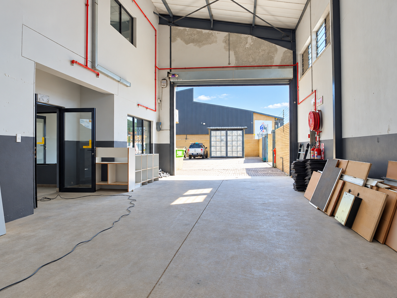 Spacious industrial garage unit featuring high ceilings with exposed steel trusses, concrete flooring, and integrated fire safety equipment, offering versatile workspace potential.