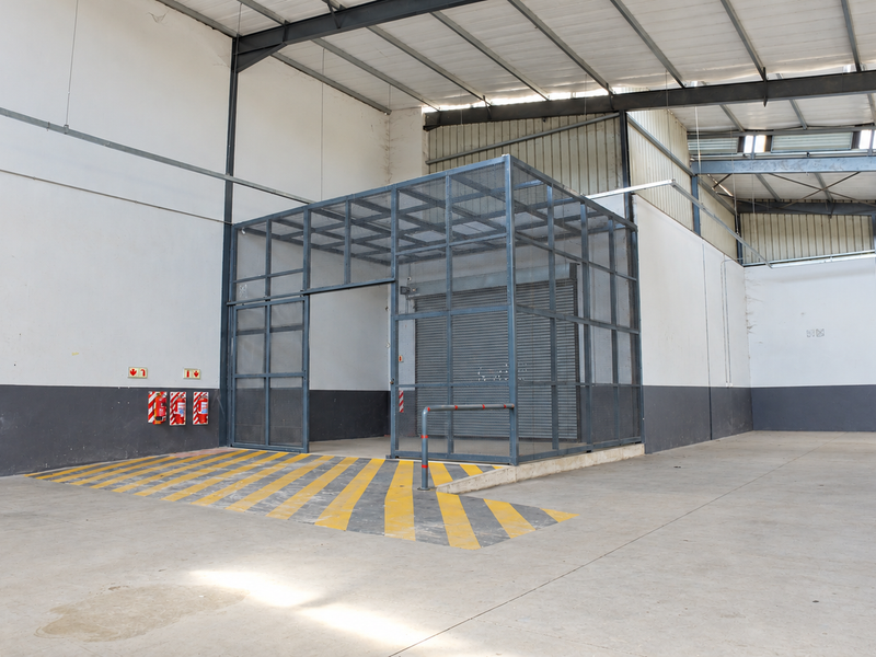Spacious industrial warehouse interior featuring a secure steel mesh cage, concrete flooring, and high-clearance exposed roof trusses, suitable for storage or secure operations.