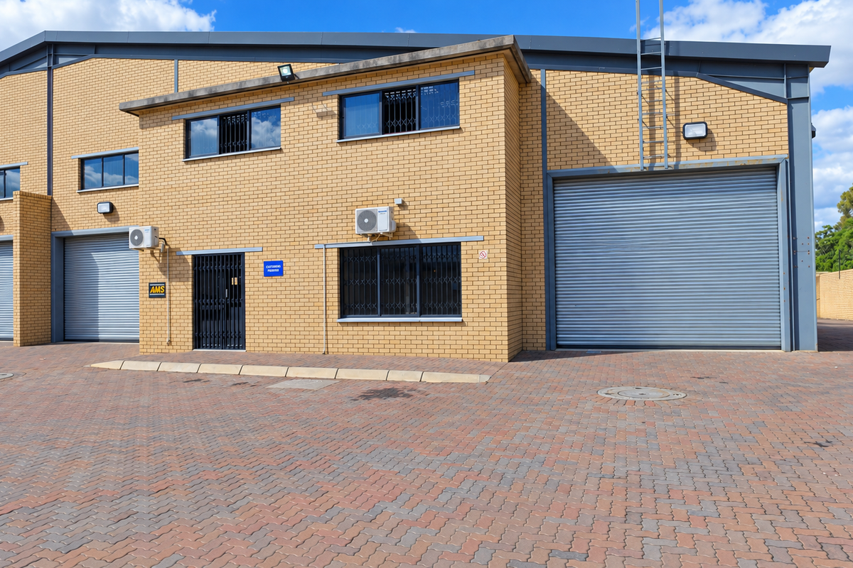 Front elevation of an industrial warehouse facility featuring multiple roller shutter doors, brick construction, and paved exterior access area.