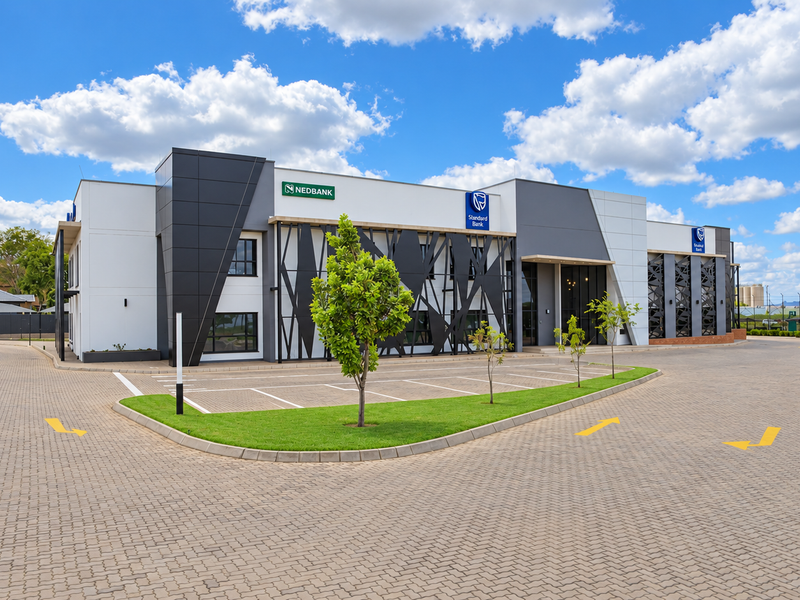 Modern commercial office building featuring contemporary facade cladding, decorative metal screens, and a spacious paved parking area with landscaped surroundings.