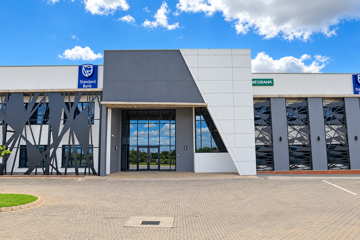 Modern commercial office building facade featuring contemporary architectural design, glass entrance, and decorative metal screening with paved parking area.