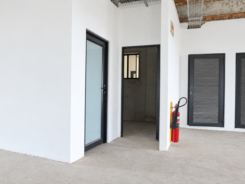 An open-plan office space in shell condition featuring exposed ceiling cable trays, concrete flooring, and multiple access doors.