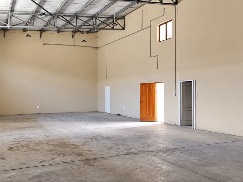 Spacious industrial utility area featuring high ceilings with exposed steel trusses, concrete flooring, and multiple access points, suitable for storage or workshop use.