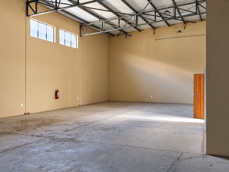 Spacious industrial utility area featuring high-level windows, exposed steel roof trusses, and durable concrete flooring, suitable for storage or workshop use.