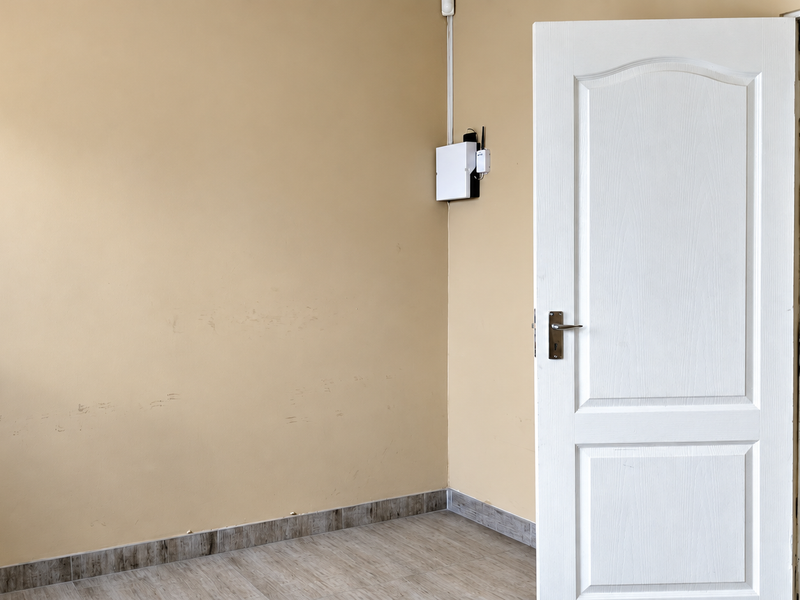 An empty hallway featuring tiled flooring and a white internal door, showing minor scuff marks on the wall surface.