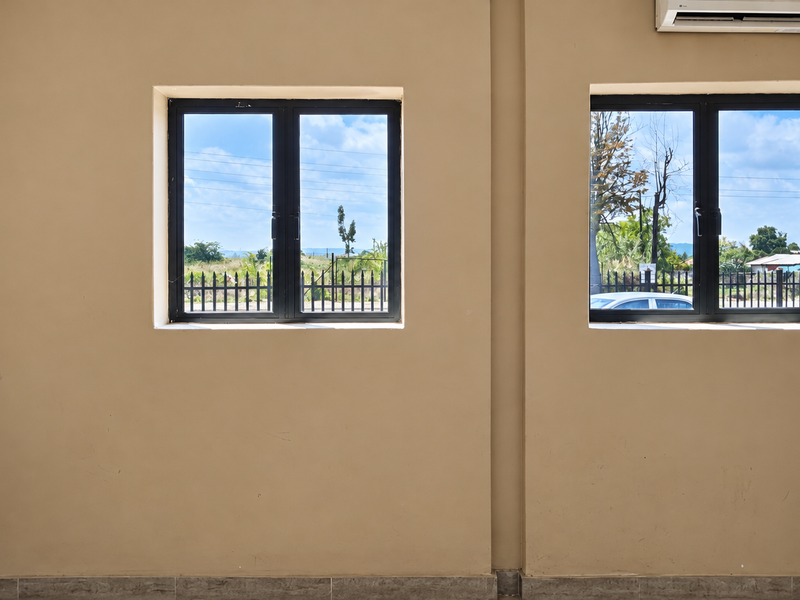 An empty office space featuring dual windows with black aluminium frames and a wall-mounted air conditioning unit.