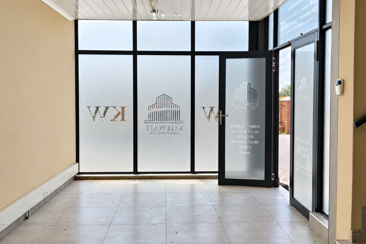 A bright and professional industrial entrance area featuring large glass storefront windows, frosted glass doors, and clean tiled flooring.