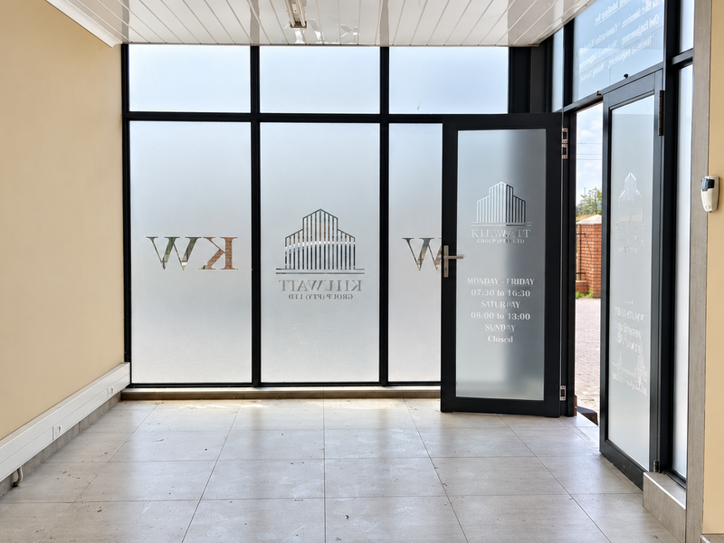 A bright and professional industrial entrance area featuring large glass storefront windows, frosted glass doors, and clean tiled flooring.