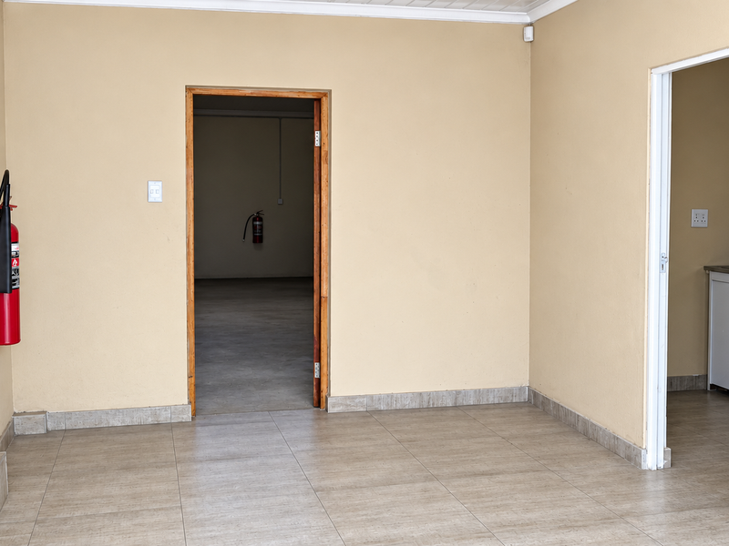 A clean, tiled utility area featuring a staircase, fire safety equipment, and access to an adjoining room and kitchenette space.