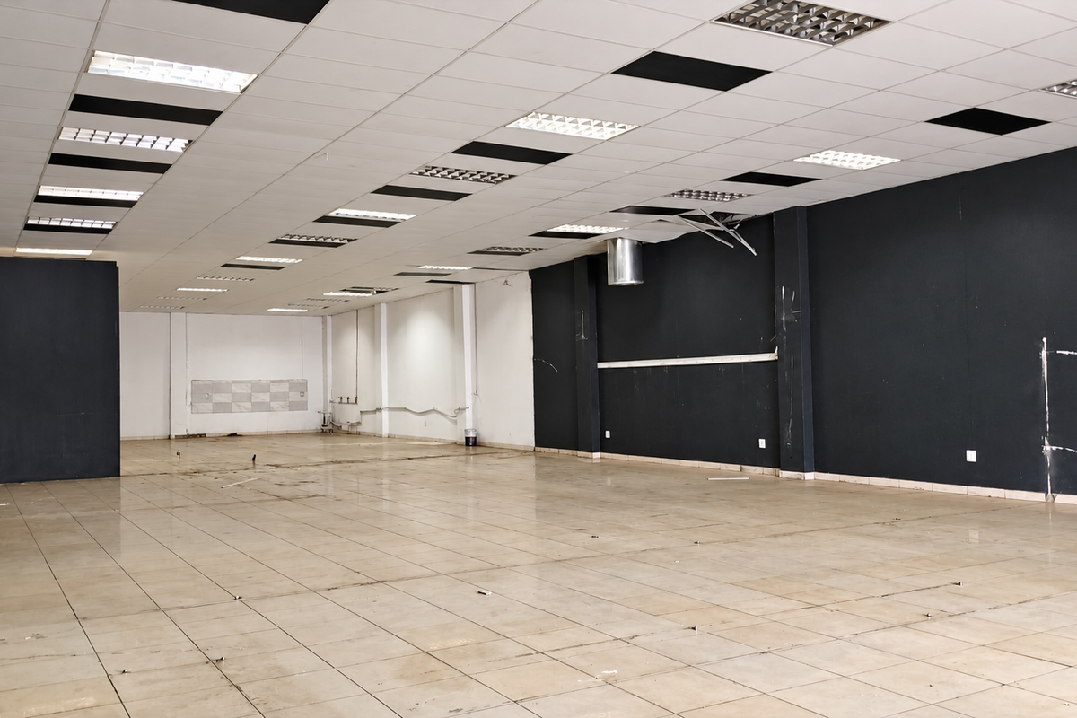 A large, vacant open-plan retail space featuring tiled flooring, a suspended ceiling with recessed lighting, and dark-painted feature walls.