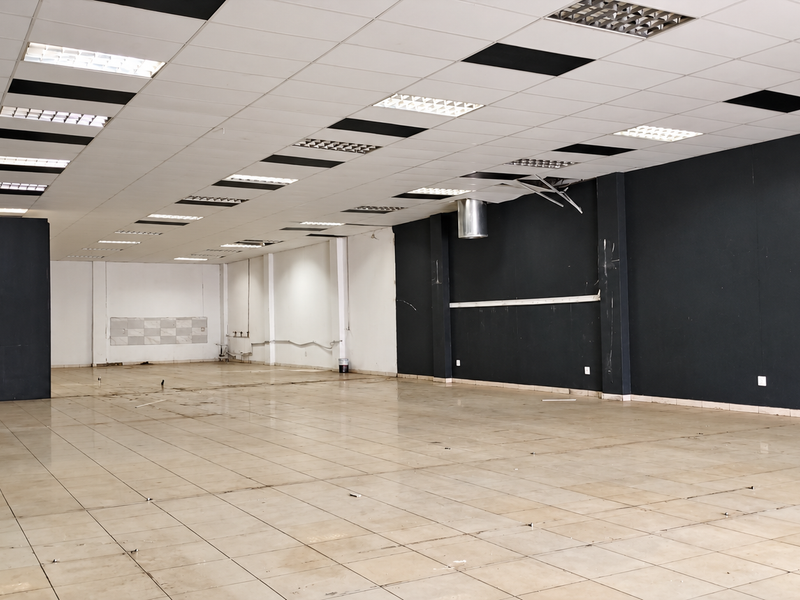 A large, vacant open-plan retail space featuring tiled flooring, a suspended ceiling with recessed lighting, and dark-painted feature walls.
