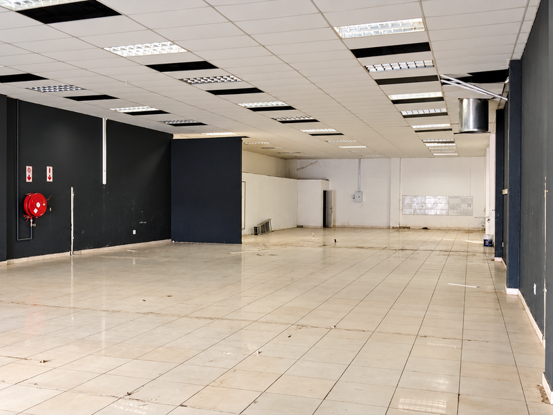 Spacious open-plan retail area featuring tiled flooring, a suspended ceiling with recessed lighting, and a wall-mounted fire hose reel.