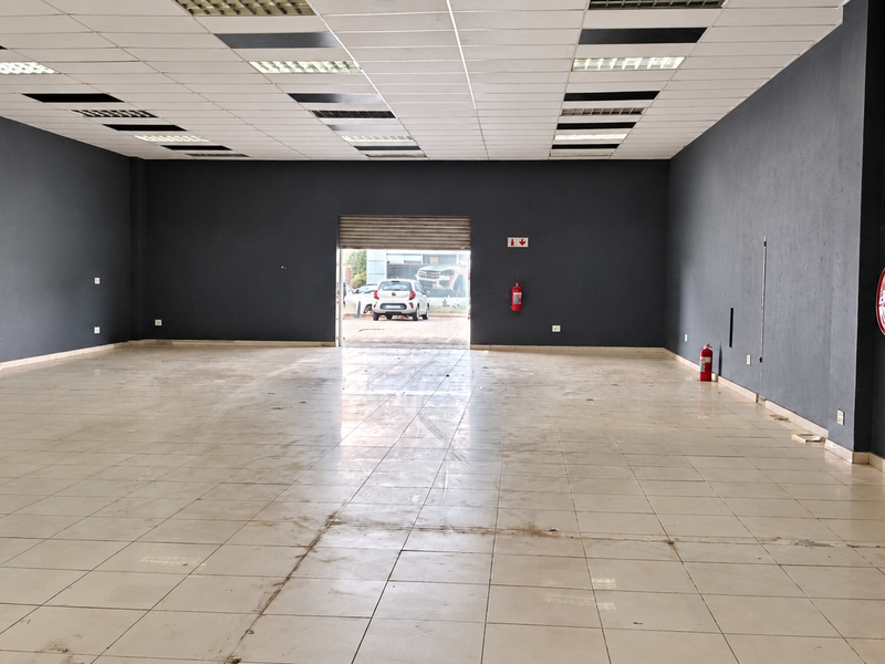 Spacious open-plan retail unit featuring a suspended ceiling, recessed lighting, tiled flooring, and integrated fire safety equipment with a rear roller shutter door.