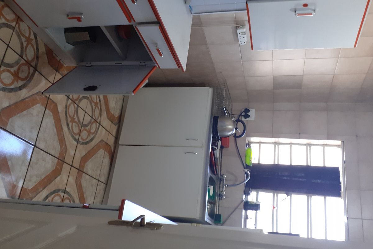 A dated kitchen featuring built-in cabinetry, tiled walls, and patterned floor tiles, requiring modernization to improve functionality and aesthetic appeal.