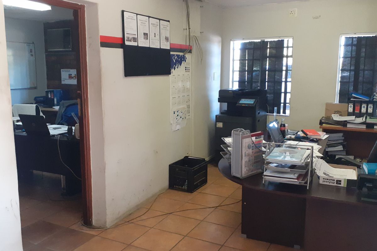 A functional commercial office space featuring tiled flooring, security-barred windows, and multiple workstations, currently showing signs of wear and tear.