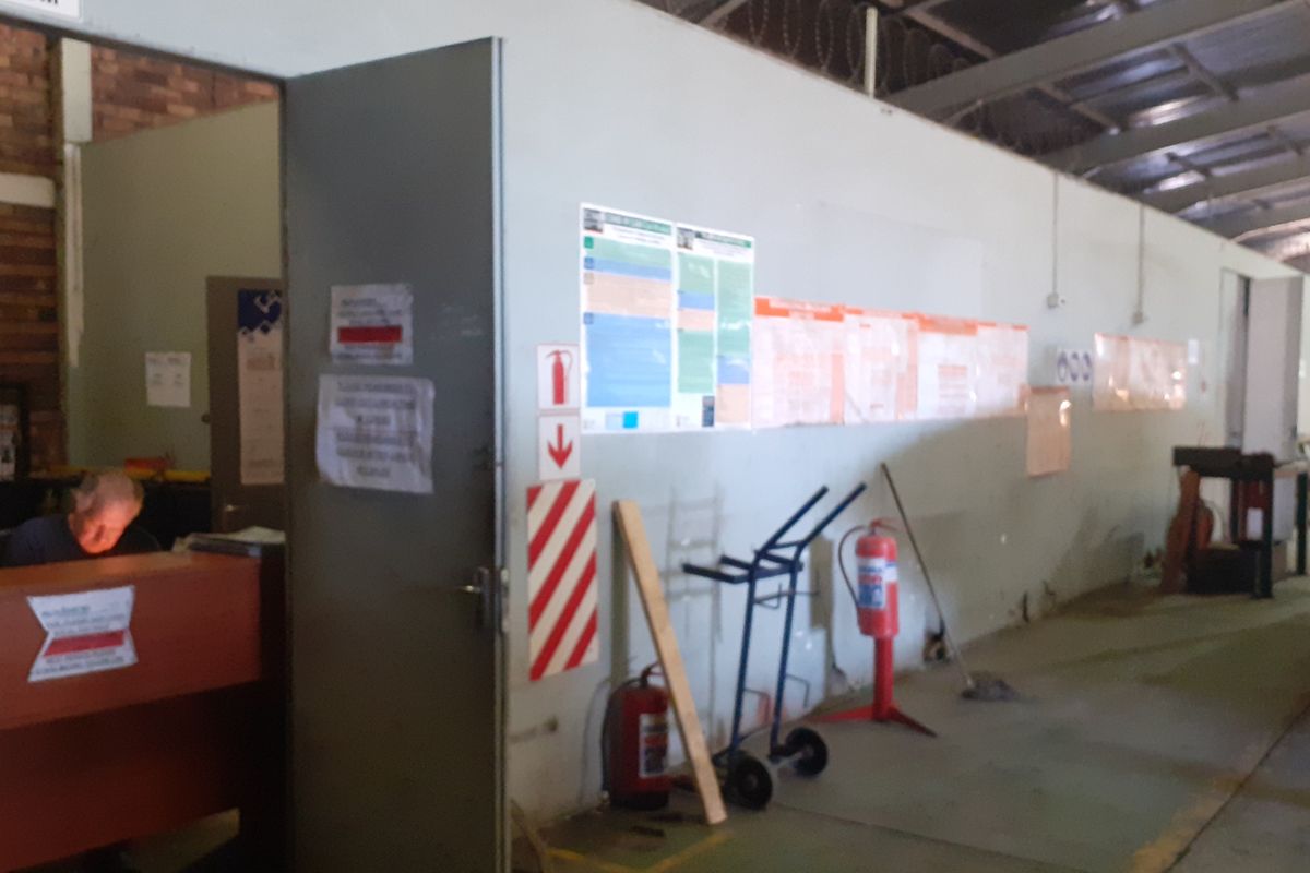 A functional industrial utility space featuring exposed steel roof trusses, concrete flooring, and wall-mounted safety equipment within a commercial warehouse setting.