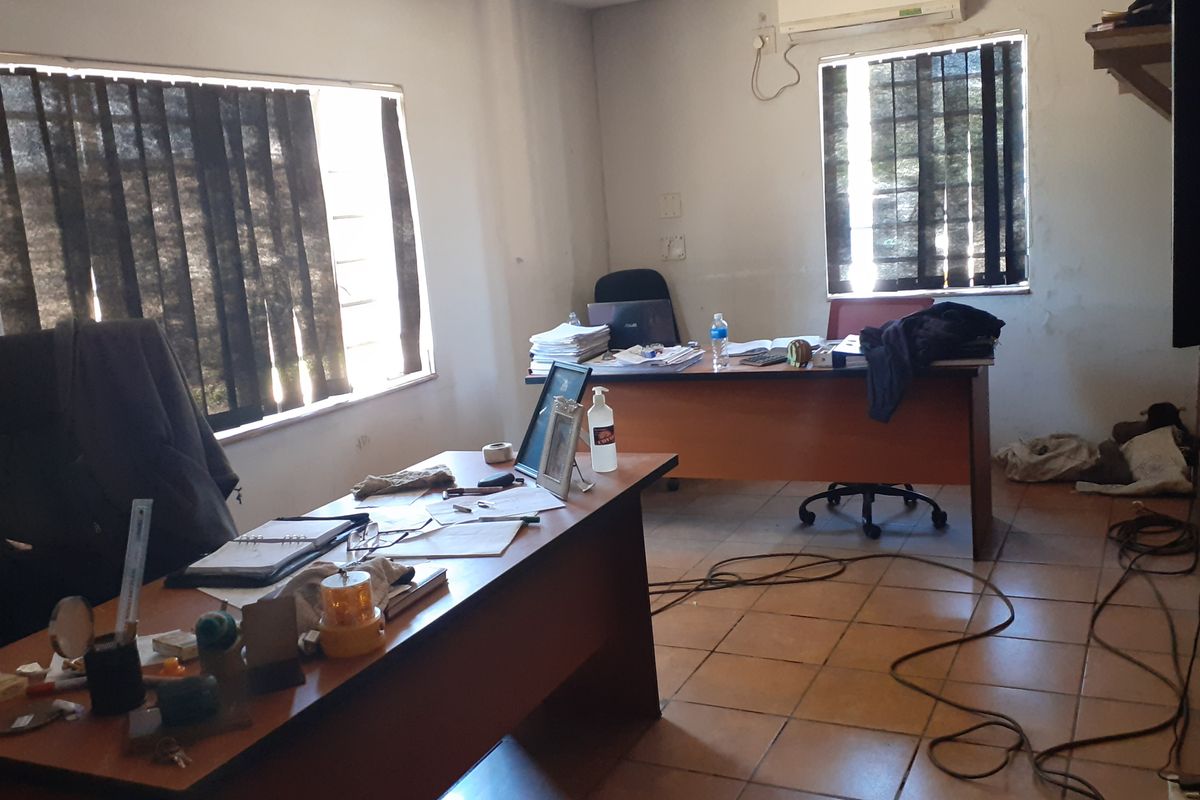 A functional commercial office space featuring tiled flooring, vertical window blinds, and a wall-mounted air conditioning unit.
