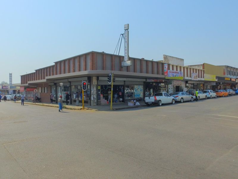 A street-level view of a commercial corner building featuring multiple storefronts and prominent signage in a busy urban setting.