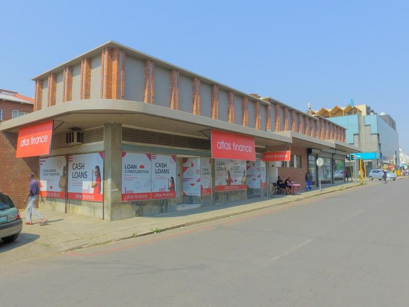 Street-level view of a commercial building featuring a brick facade, concrete awning, and large display windows currently utilized for retail signage.