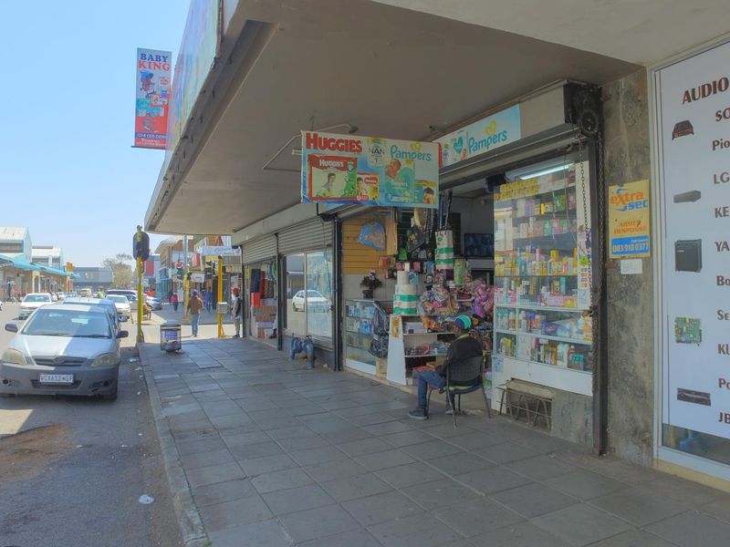 Street-level view of a commercial shopfront featuring a display window, security shutter, and covered walkway in a busy urban retail area.