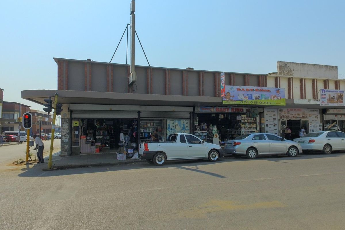 Street-level view of a commercial retail building featuring metal roller shutter entrances and prominent signage along a busy urban thoroughfare.