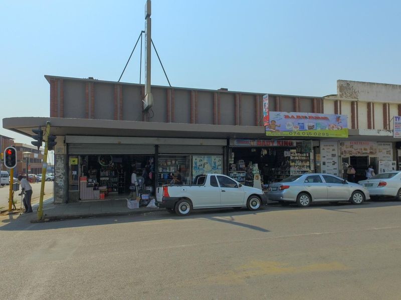 Street-level view of a commercial retail building featuring metal roller shutter entrances and prominent signage along a busy urban thoroughfare.